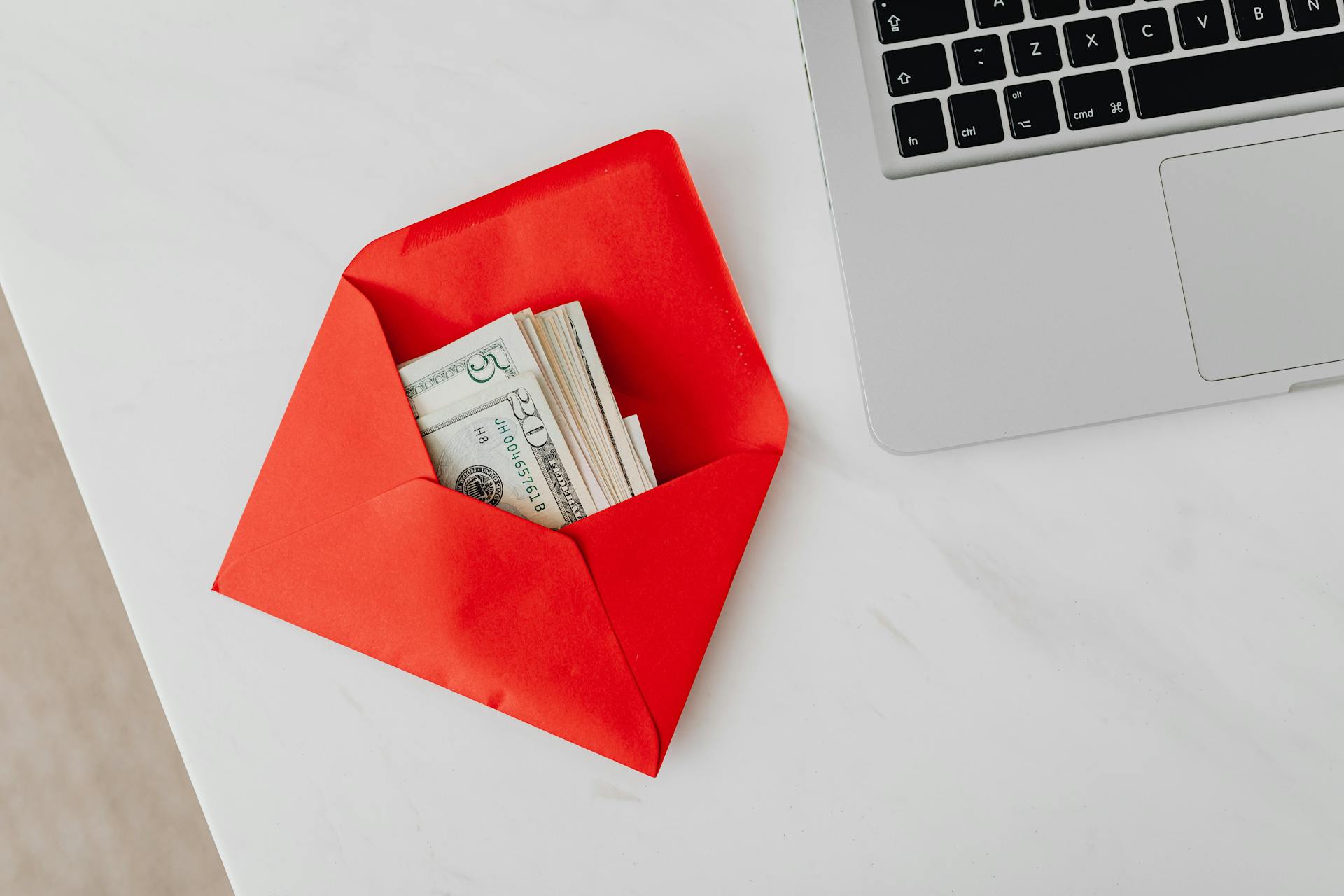 money inside red envelope next to laptop on table